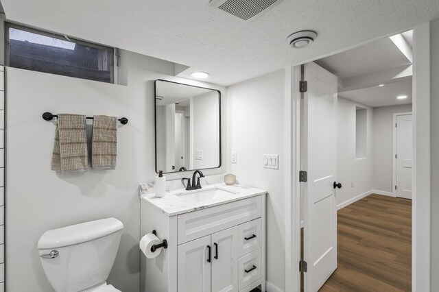 bathroom with visible vents, toilet, vanity, a textured ceiling, and wood finished floors