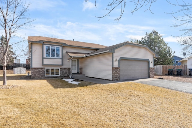 split level home featuring brick siding, aphalt driveway, a garage, and fence