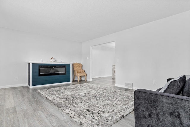 living area featuring a glass covered fireplace, wood finished floors, visible vents, and baseboards