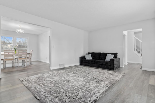 living area with a notable chandelier, visible vents, wood finished floors, baseboards, and stairs