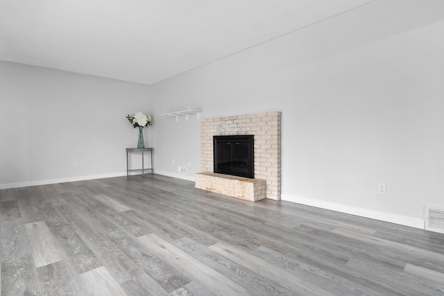 unfurnished living room with visible vents, a fireplace, baseboards, and wood finished floors