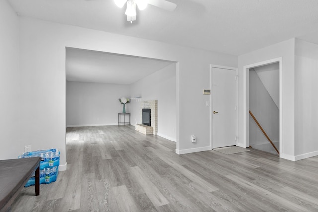 unfurnished living room with a brick fireplace, ceiling fan, baseboards, and wood finished floors