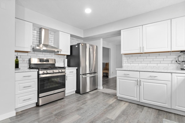 kitchen with appliances with stainless steel finishes, wall chimney range hood, baseboards, light wood-type flooring, and backsplash