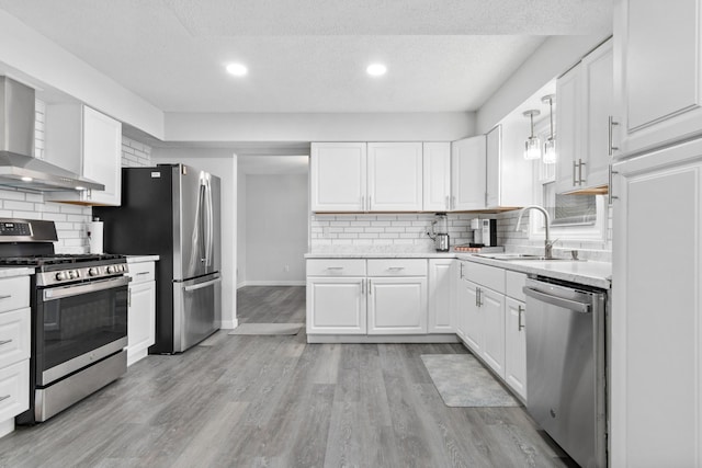 kitchen featuring stainless steel appliances, wall chimney exhaust hood, a sink, decorative backsplash, and white cabinets