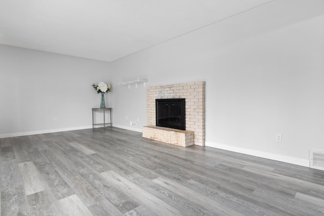 unfurnished living room featuring wood finished floors, a brick fireplace, and baseboards