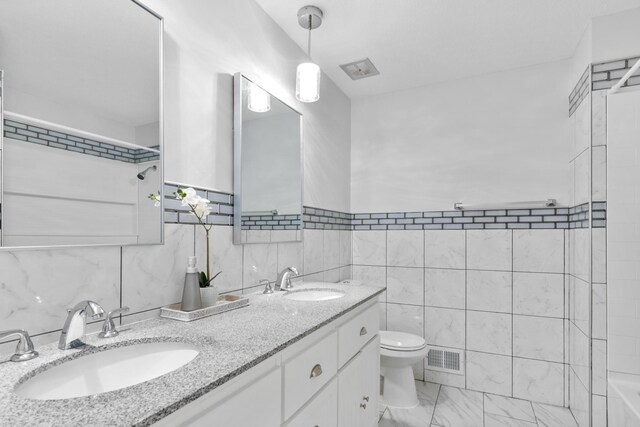 bathroom featuring tile walls, toilet, double vanity, marble look tile flooring, and a shower