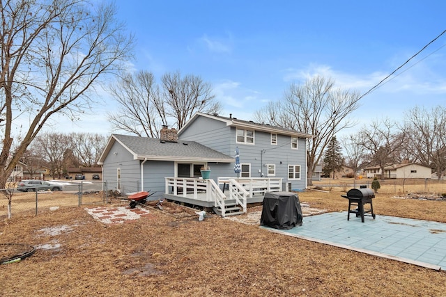 rear view of house featuring a deck, fence, a chimney, a patio area, and roof with shingles