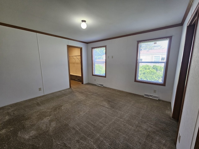 spare room featuring dark colored carpet, ornamental molding, and visible vents