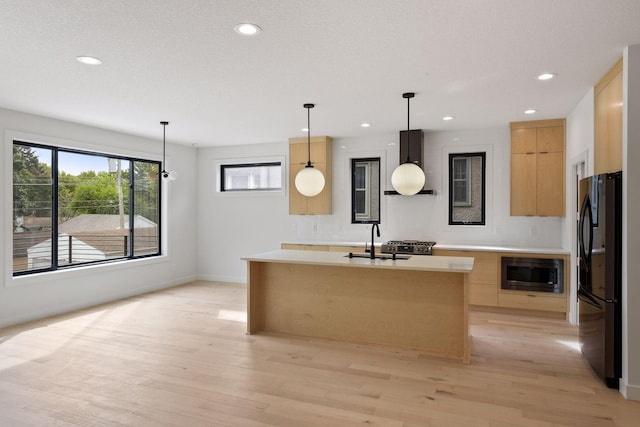 kitchen featuring freestanding refrigerator, stainless steel microwave, wall chimney exhaust hood, and modern cabinets