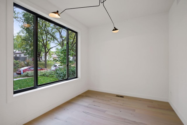 empty room featuring light wood finished floors, baseboards, and visible vents