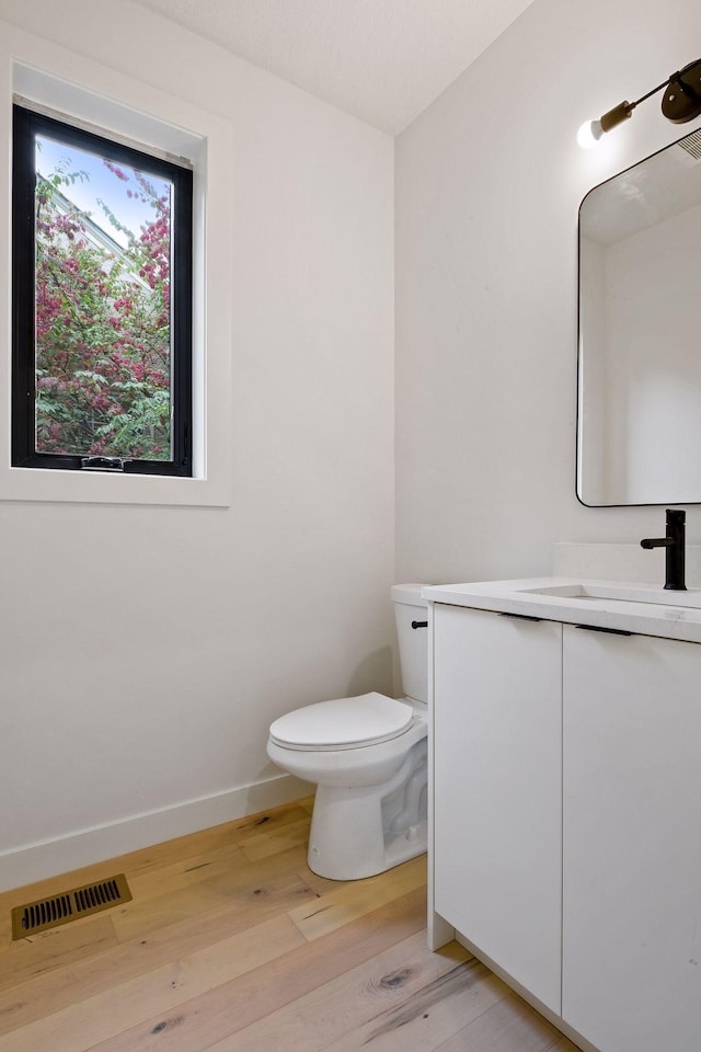 half bath featuring visible vents, hardwood / wood-style floors, toilet, vanity, and baseboards