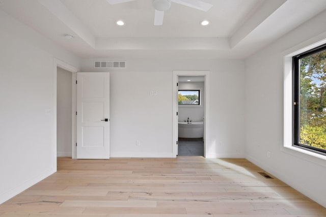 spare room with light wood-type flooring, a raised ceiling, visible vents, and baseboards