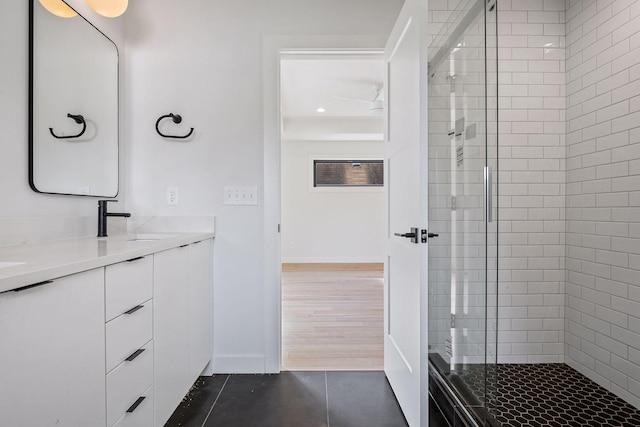 bathroom with double vanity, a sink, a shower stall, tile patterned flooring, and baseboards