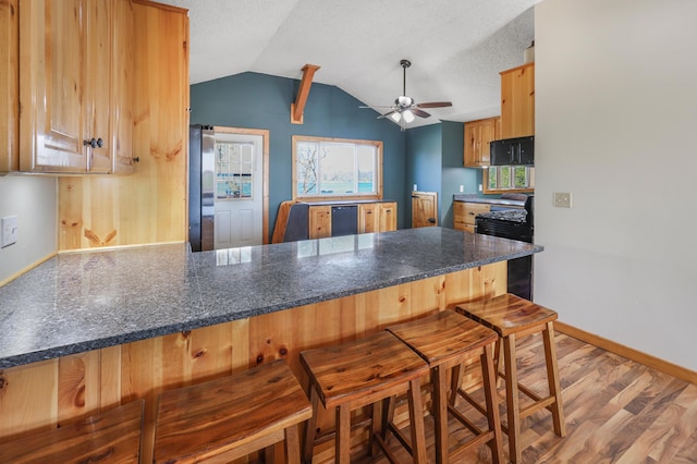 kitchen with a ceiling fan, baseboards, freestanding refrigerator, a peninsula, and lofted ceiling