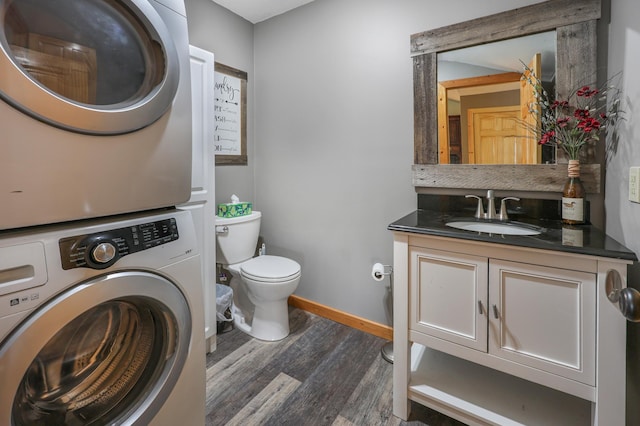 bathroom with vanity, wood finished floors, toilet, baseboards, and stacked washing maching and dryer