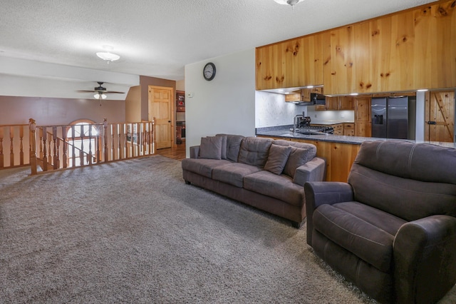 carpeted living room featuring a sink, a ceiling fan, and a textured ceiling