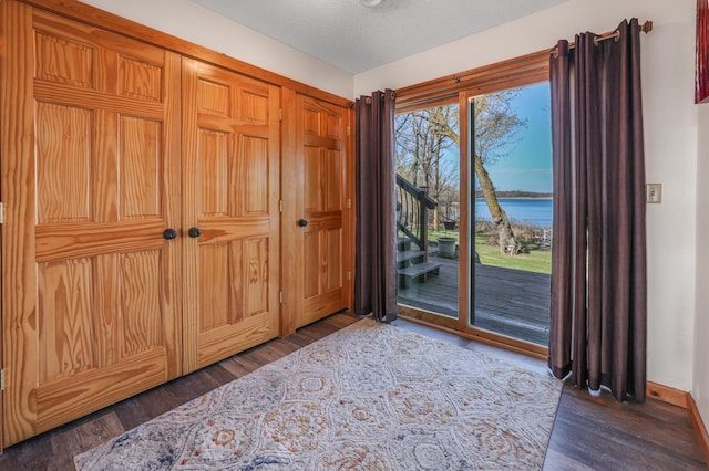 interior space featuring dark wood-type flooring, a textured ceiling, baseboards, and a water view