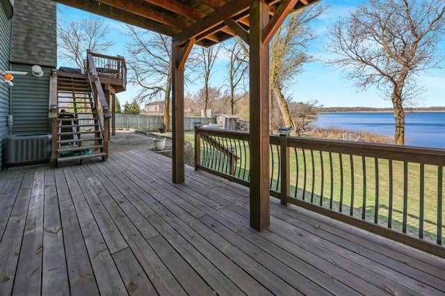 deck featuring central AC, stairway, a fenced backyard, a water view, and a yard