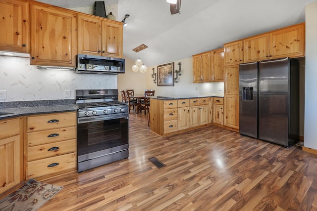 kitchen featuring visible vents, a peninsula, lofted ceiling, dark countertops, and stainless steel appliances