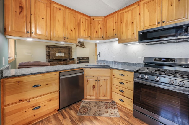 kitchen featuring decorative backsplash, appliances with stainless steel finishes, light wood-type flooring, a sink, and a peninsula