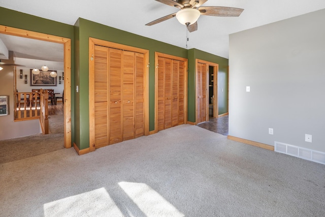 unfurnished bedroom with visible vents, multiple closets, baseboards, ceiling fan, and carpet