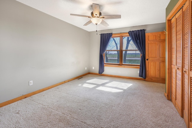 unfurnished bedroom featuring carpet floors, a ceiling fan, baseboards, and a closet