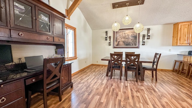 dining space featuring light wood-style floors, baseboards, a textured ceiling, and lofted ceiling