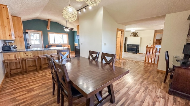 dining space with a ceiling fan, a textured ceiling, lofted ceiling, and light wood-style floors