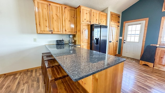 kitchen with light wood finished floors, a peninsula, a kitchen bar, refrigerator with ice dispenser, and vaulted ceiling
