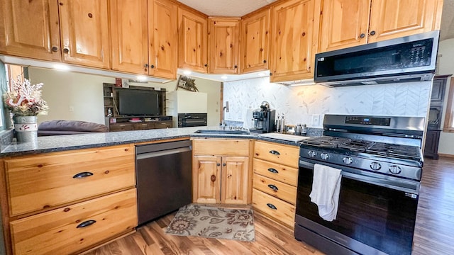 kitchen featuring open floor plan, tasteful backsplash, a sink, light wood finished floors, and appliances with stainless steel finishes