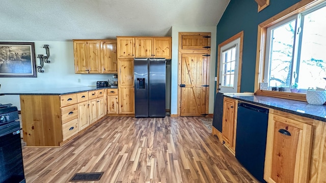 kitchen with dark countertops, a textured ceiling, stainless steel fridge, and light wood-style floors