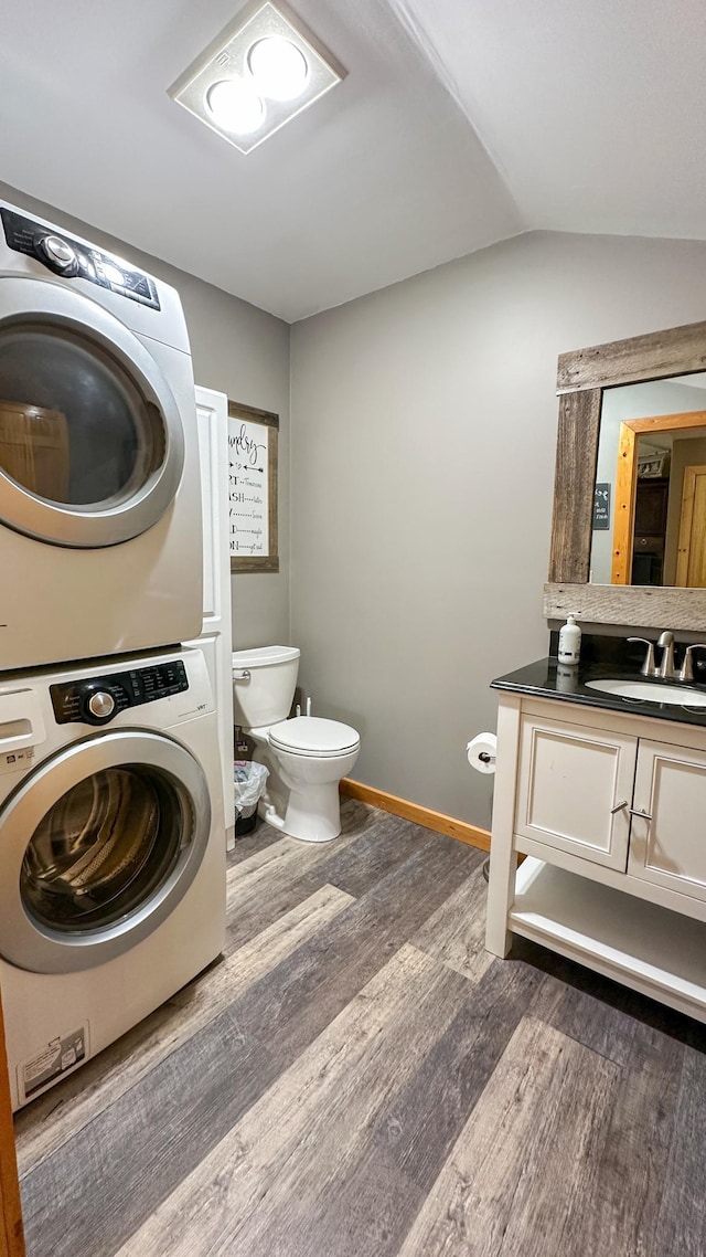 bathroom with stacked washer and dryer, wood finished floors, vanity, toilet, and lofted ceiling