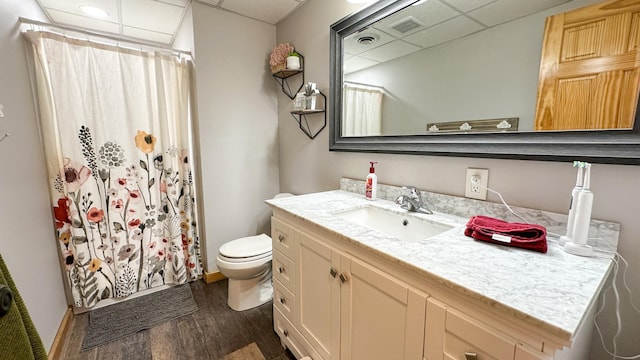 bathroom with wood finished floors, vanity, baseboards, toilet, and a drop ceiling