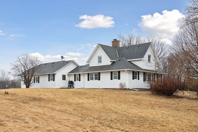 rear view of house with a shingled roof, a lawn, and a chimney