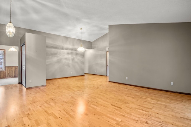 spare room featuring lofted ceiling, a wainscoted wall, light wood-type flooring, and a notable chandelier