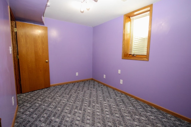 unfurnished room featuring dark carpet and baseboards