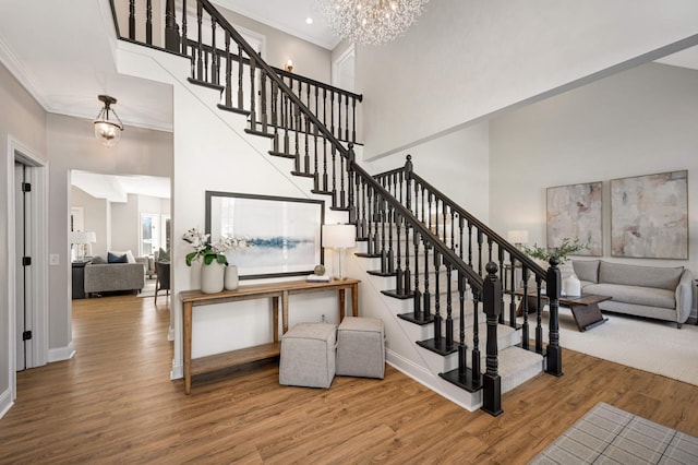 staircase featuring baseboards, ornamental molding, wood finished floors, an inviting chandelier, and a high ceiling