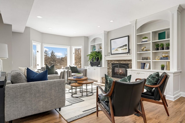 living room featuring light wood-type flooring, a brick fireplace, built in features, and recessed lighting