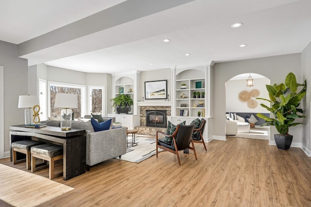 living area featuring light wood finished floors, baseboards, a brick fireplace, built in shelves, and recessed lighting