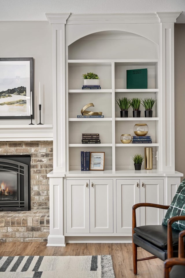 living area with light wood-type flooring, a brick fireplace, and ornate columns