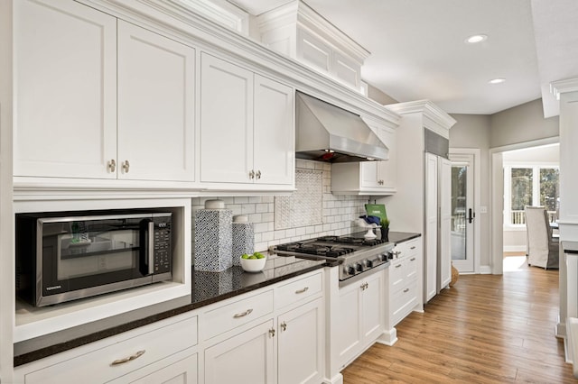 kitchen with white cabinets, wall chimney exhaust hood, appliances with stainless steel finishes, and light wood-style flooring