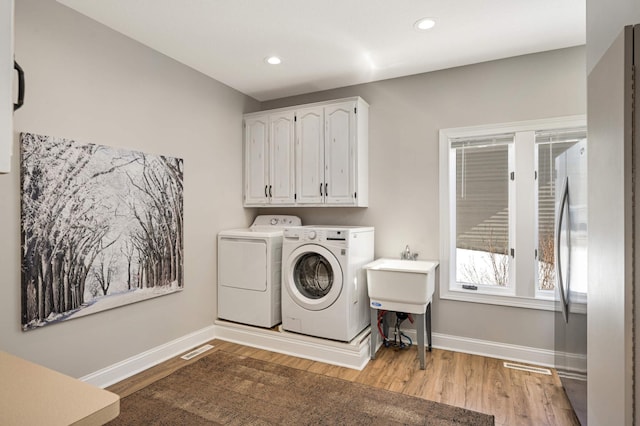 clothes washing area featuring baseboards, light wood-type flooring, cabinet space, and washer and dryer