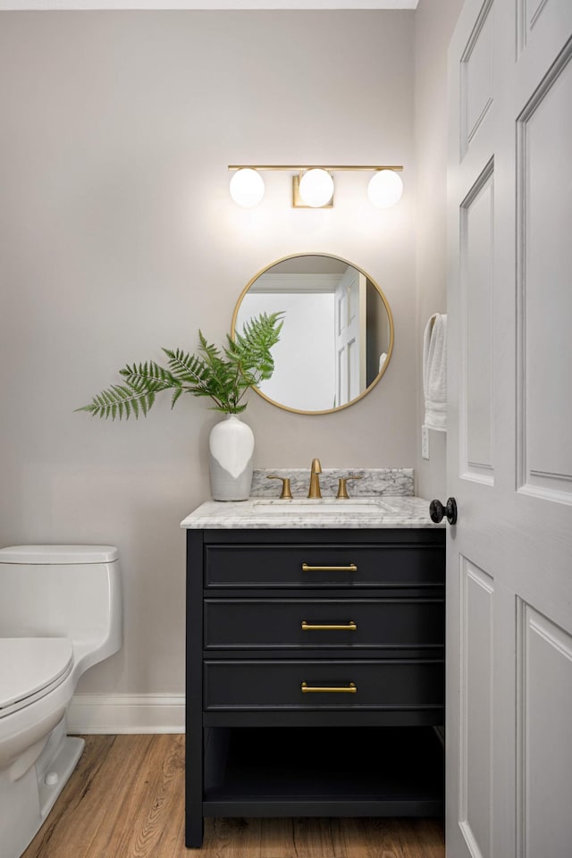 bathroom with toilet, baseboards, wood finished floors, and vanity