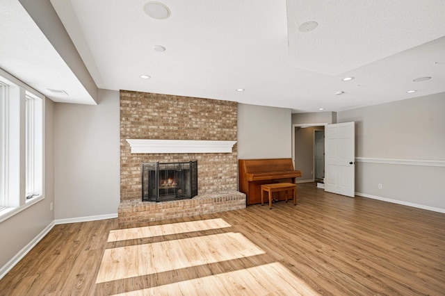 unfurnished living room with baseboards, wood finished floors, a textured ceiling, a fireplace, and recessed lighting