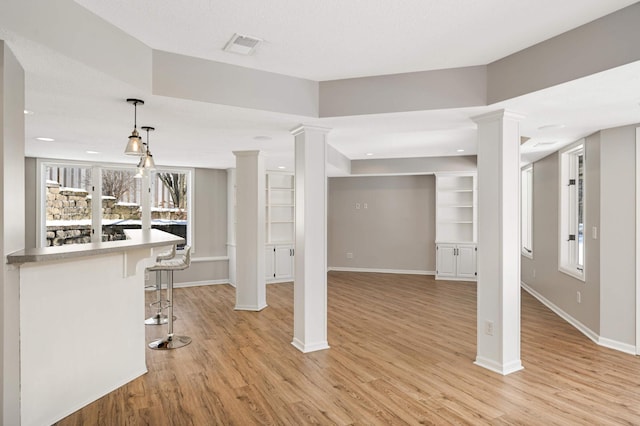 interior space featuring ornate columns, light wood-style flooring, and baseboards