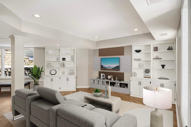 living area with recessed lighting, a raised ceiling, visible vents, wood finished floors, and ornate columns