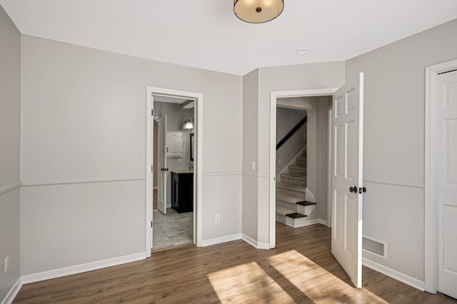 unfurnished bedroom with visible vents, ensuite bath, baseboards, and wood finished floors