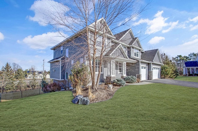 view of front facade with a front yard, fence, a garage, stone siding, and driveway