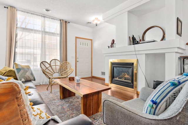 living area featuring a glass covered fireplace, visible vents, a textured ceiling, and wood finished floors