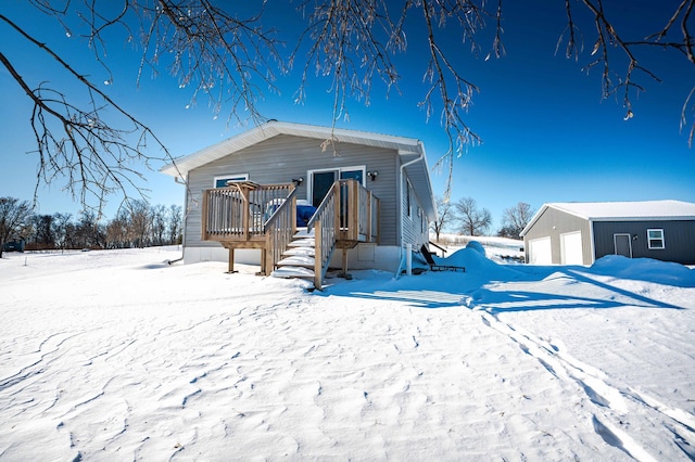 snow covered house featuring a wooden deck, a detached garage, and an outdoor structure